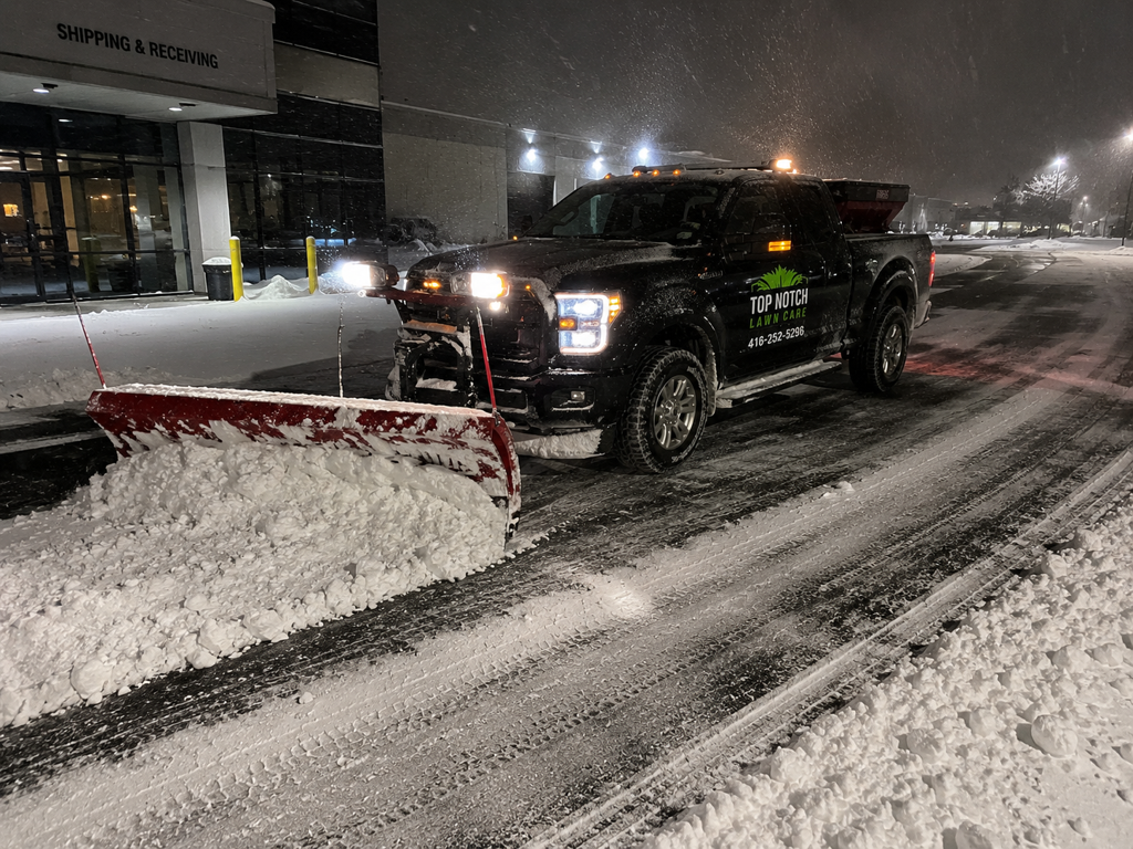 Top Notch plow truck clearing a snow-covered lot at night